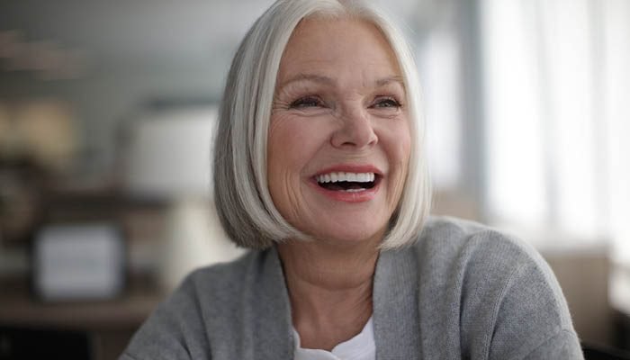 Mulher de cabelos grisalhos sorrindo, sem que o aparelho auditivo apareça